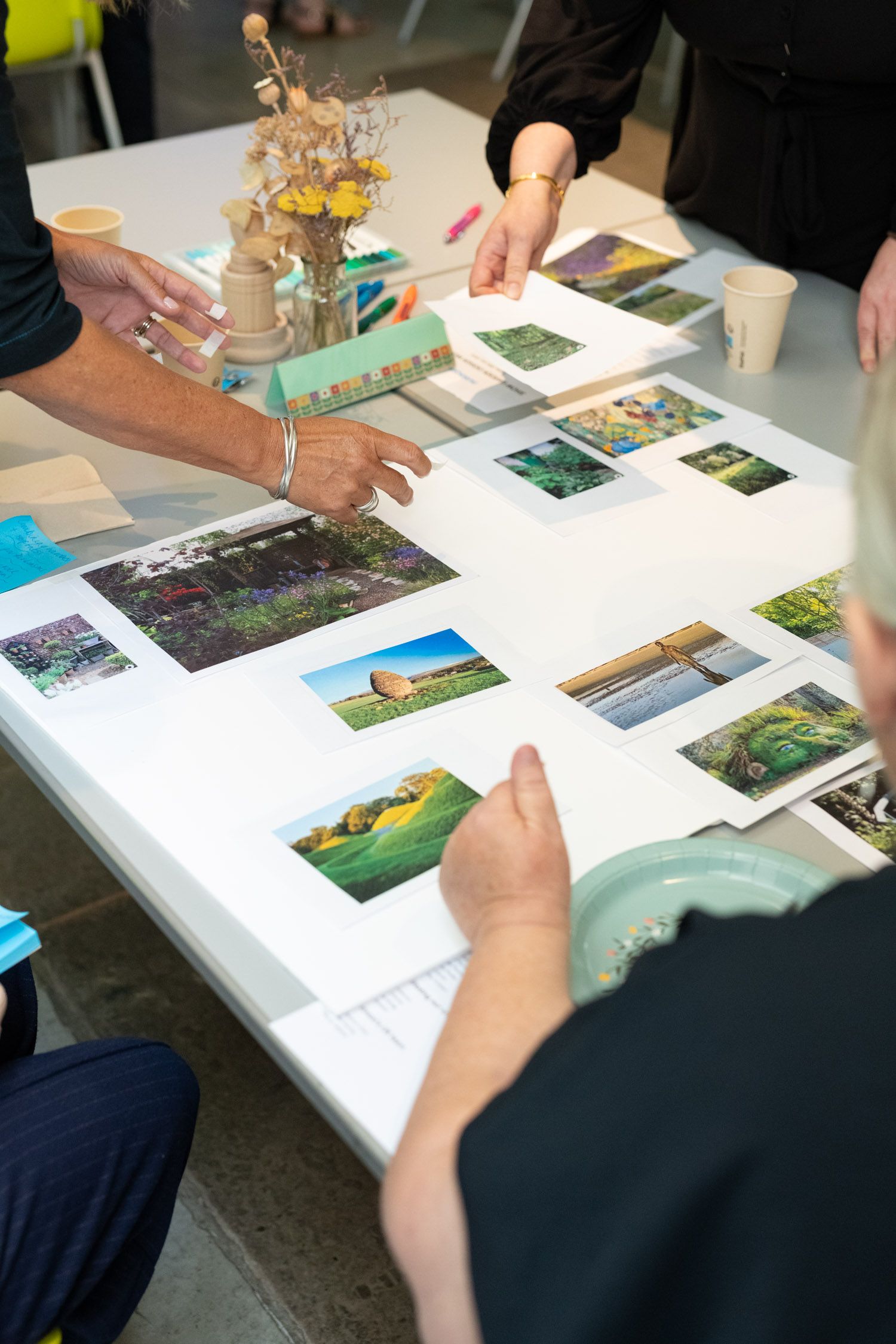 People gathered around a table reviewing printed photos and a small model during a collaborative discussion