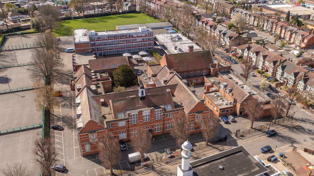 Aerial view of a brick building with several red rooftops, a green field, and residential houses.