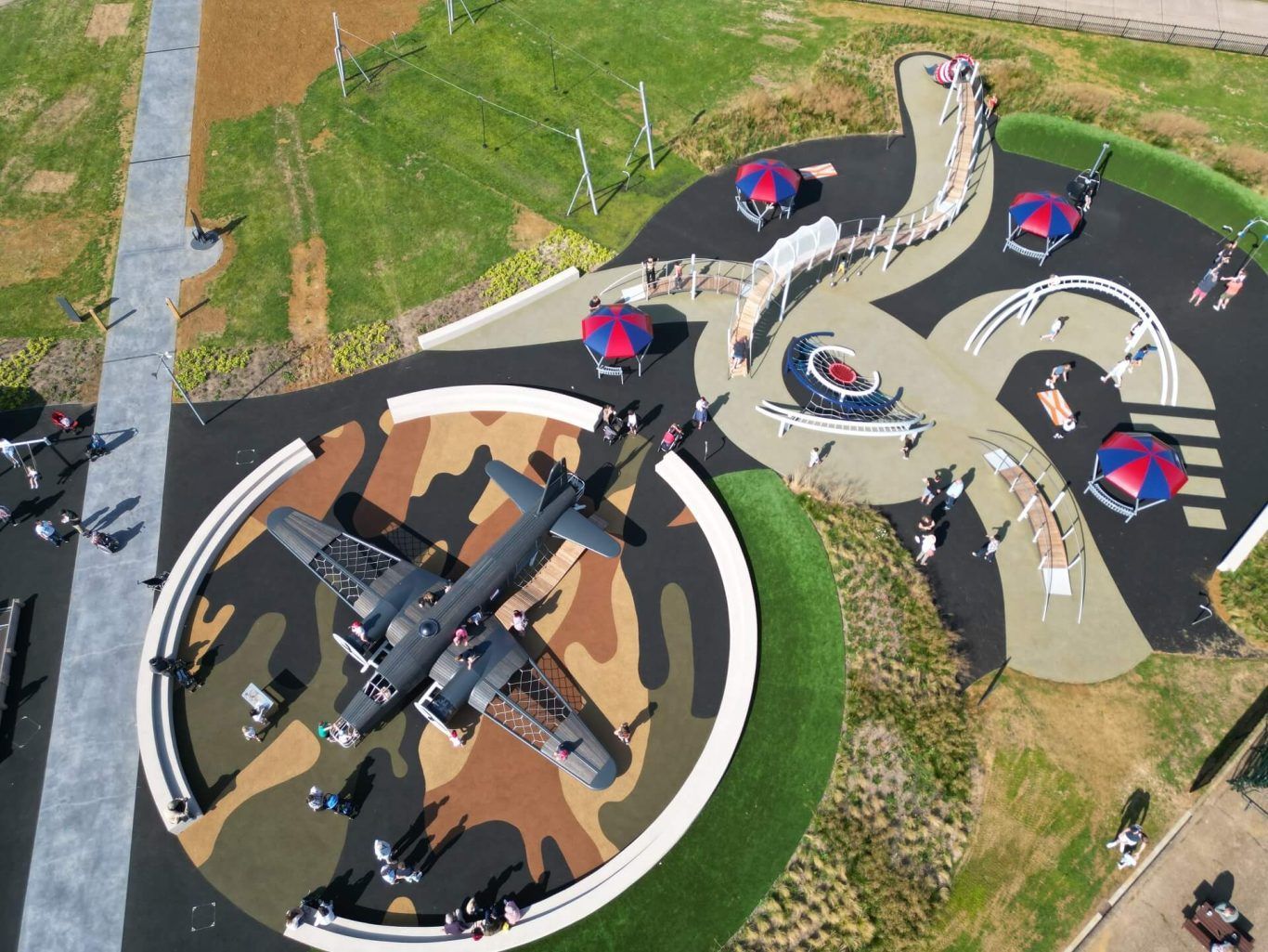 Overhead view of a playground with a plane on a camouflage base, benches, and colorful umbrellas.