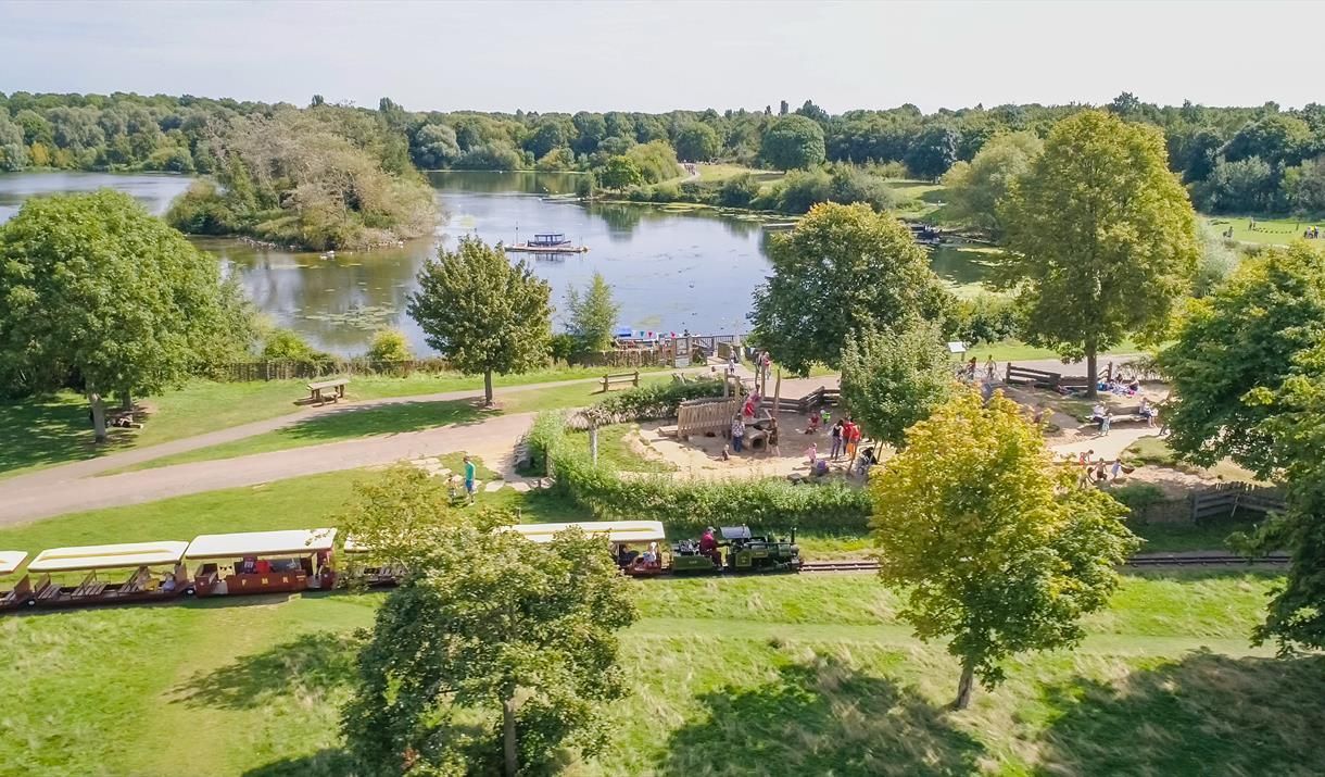 Miniature train travels past a playground and lake with a small island.