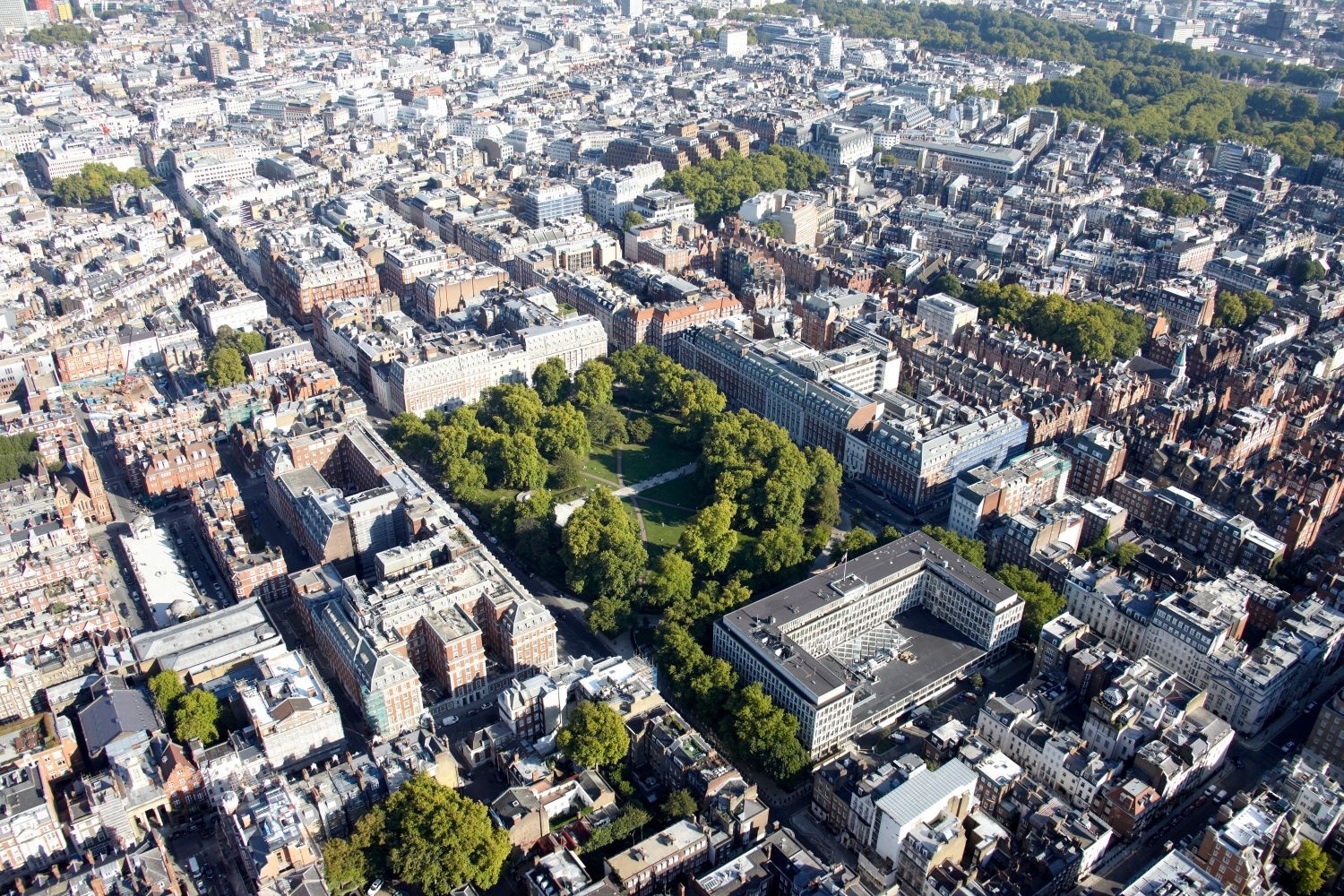 Aerial view of a city with a green park surrounded by buildings. Sunny day, rooftops visible.