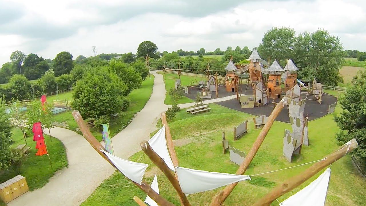 Overhead view of playground with castle-like structures, paths, trees, and a tree-like structure with white sails.