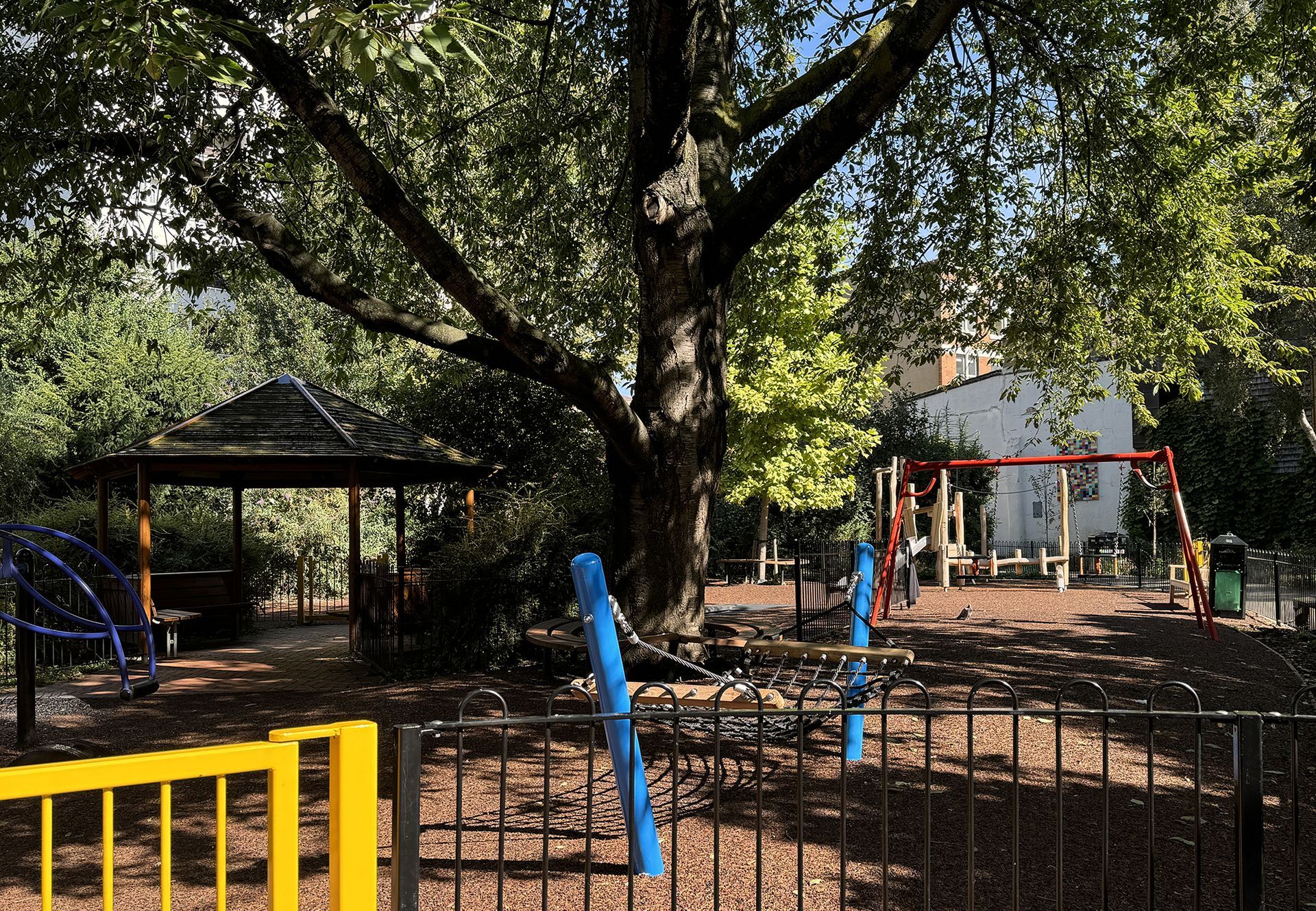 Playground with equipment, gazebo, and large tree.