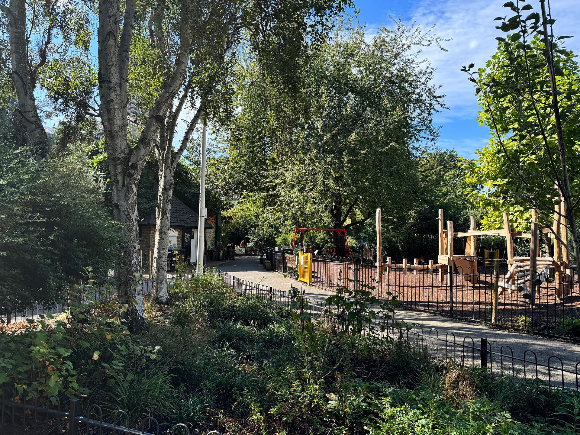 Playground with trees and play structures on a sunny day, surrounded by greenery.