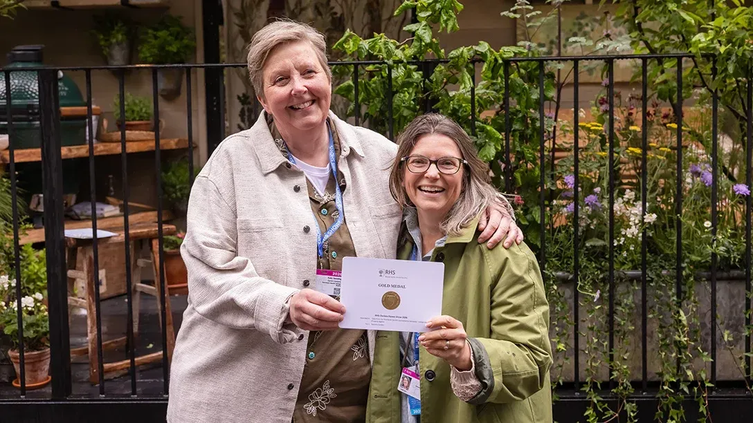 Two people holding a certificate and smiling in front of a garden fence