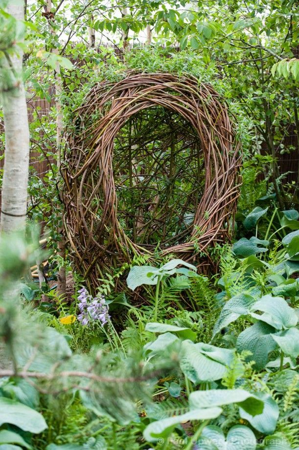 Large woven wicker arch in a lush green garden with various plants and foliage.