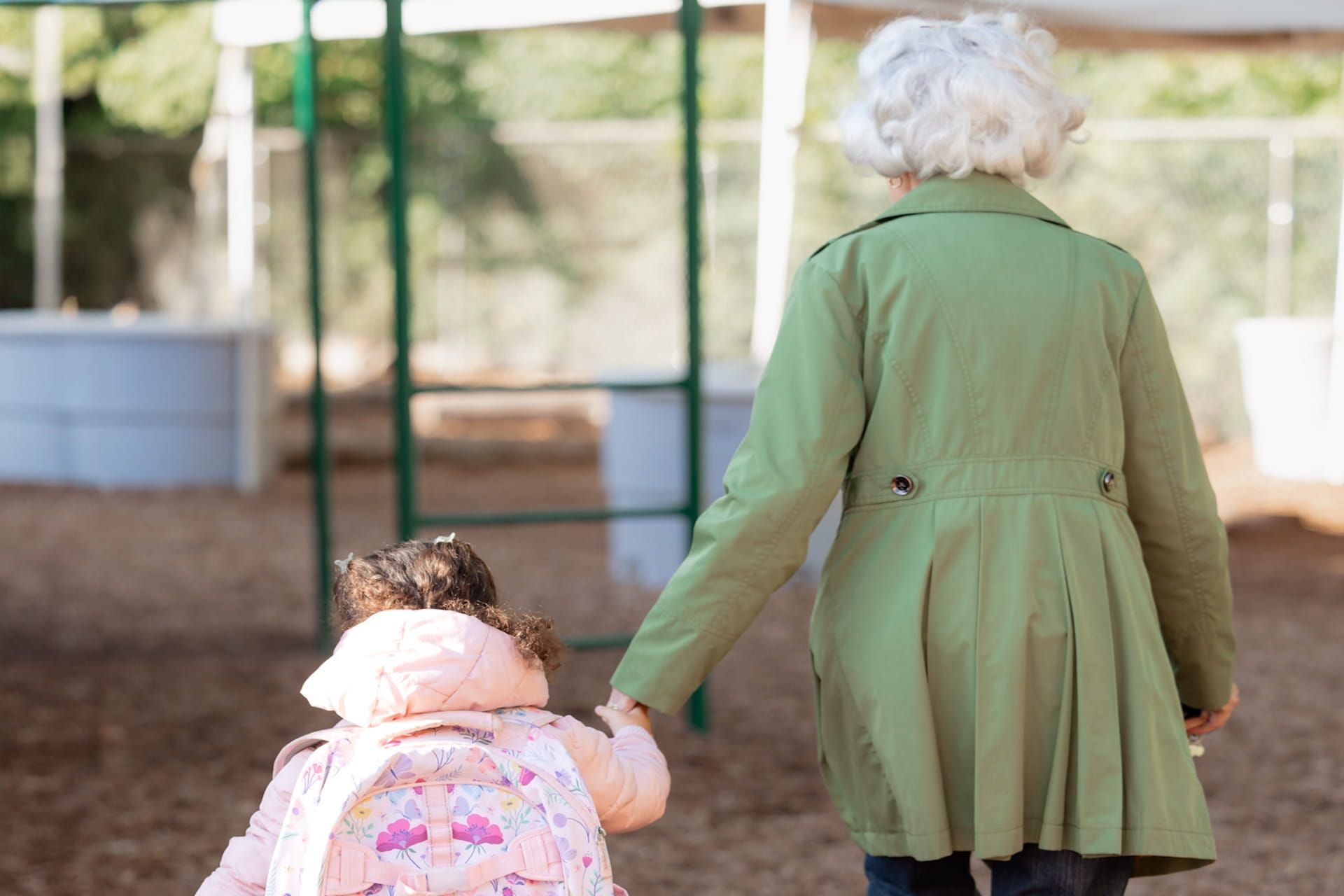 Adult walking child with backpack toward school entrance holding hands
