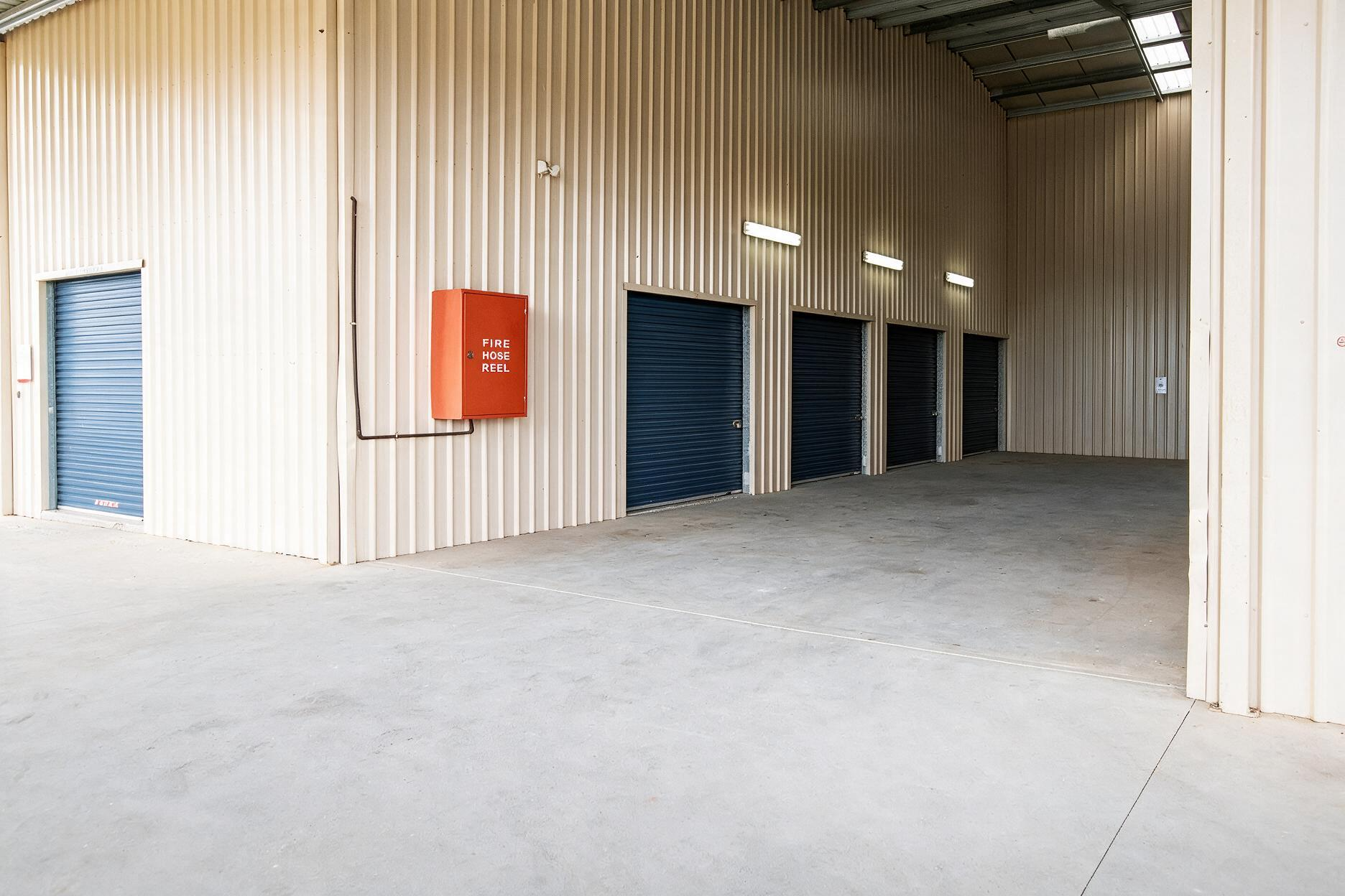 Empty warehouse interior with beige corrugated walls, blue roll-up doors, and a concrete floor