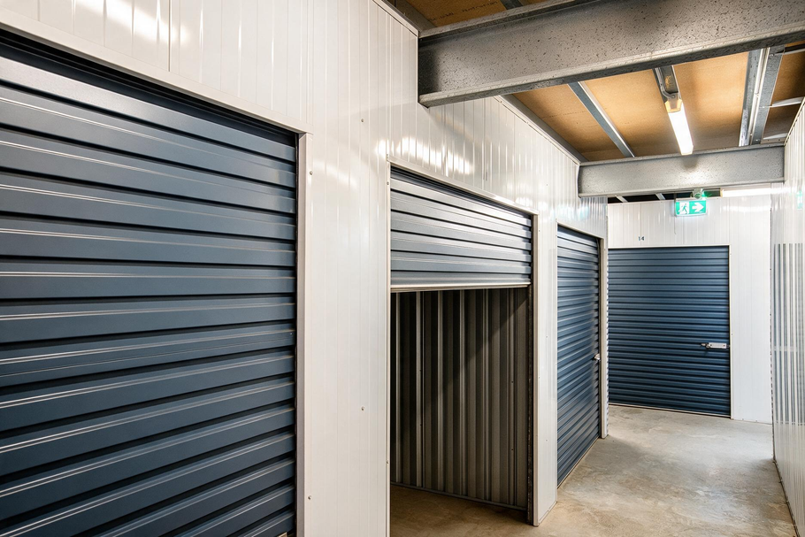 Storage hallway with gray roll-up doors and white walls under bright overhead lights