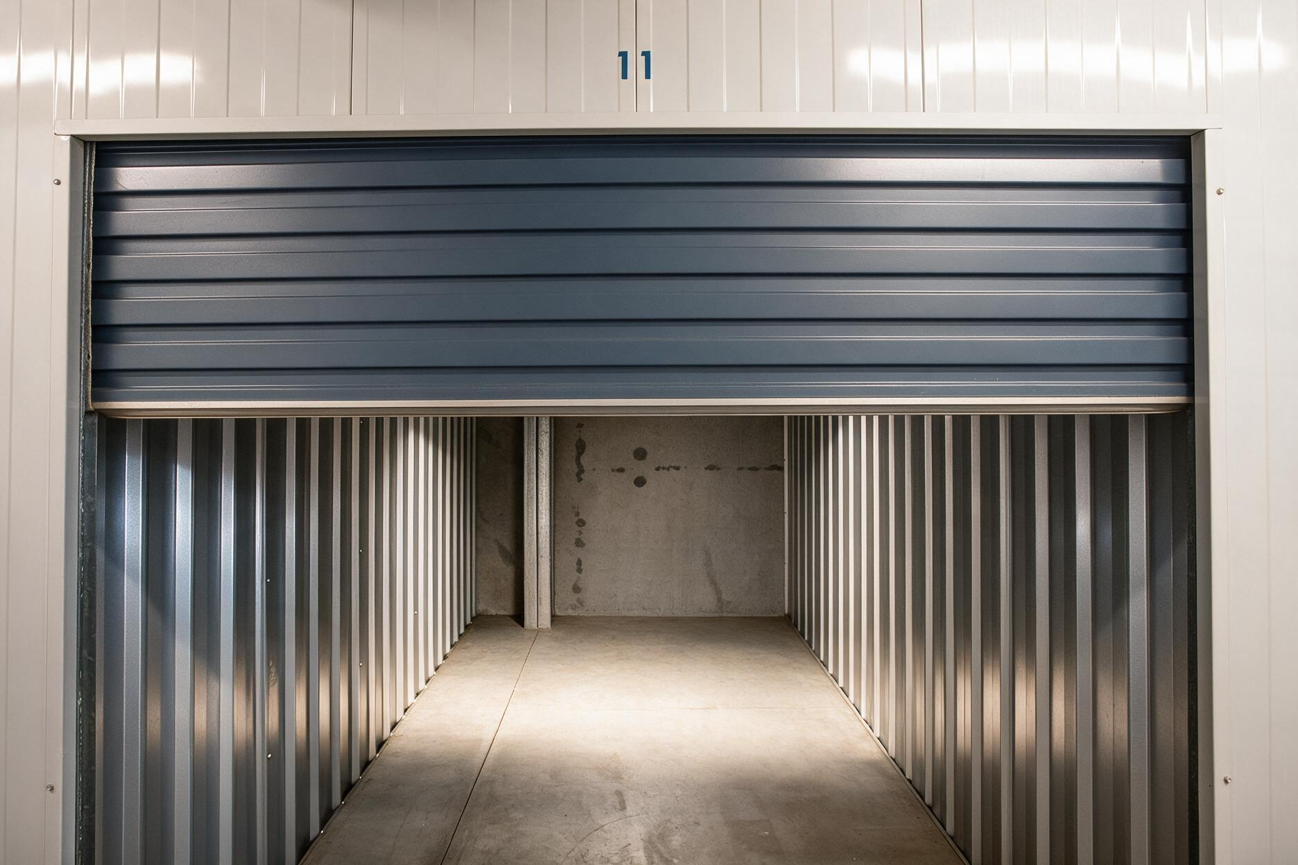 Partially closed blue roll-up door revealing a metal storage unit interior