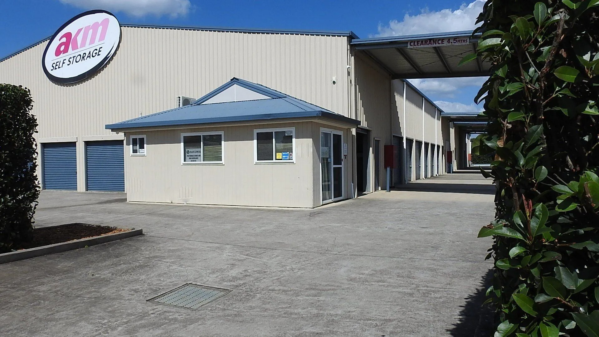 Industrial building with a white office entrance, blue roof trim, and gravel driveway