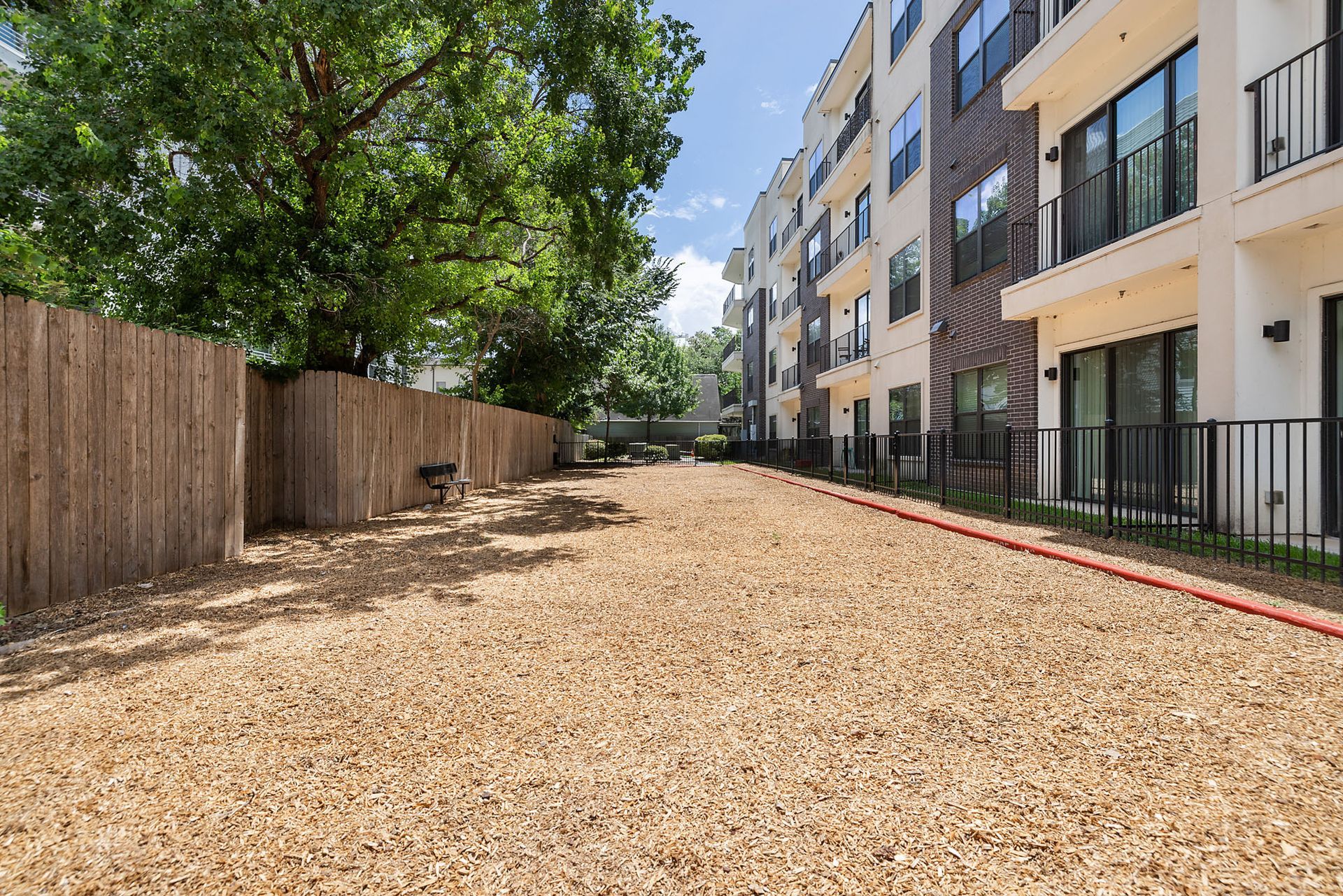Gravel path beside a wooden fence and apartment building under trees on a sunny day