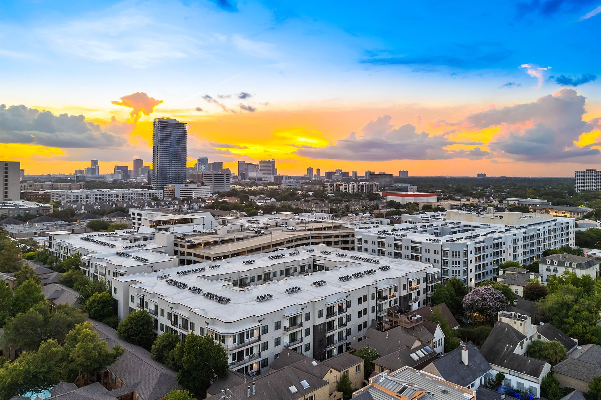 Aerial view of a modern city at sunset with white apartment buildings and a tall tower against colorful clouds