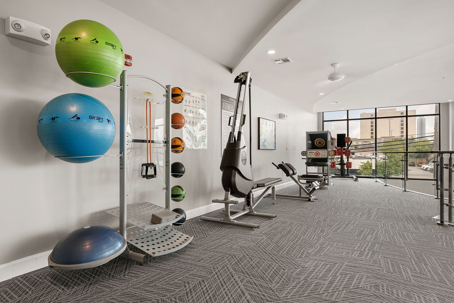Modern gym with exercise balls, cable machine, benches, and large windows