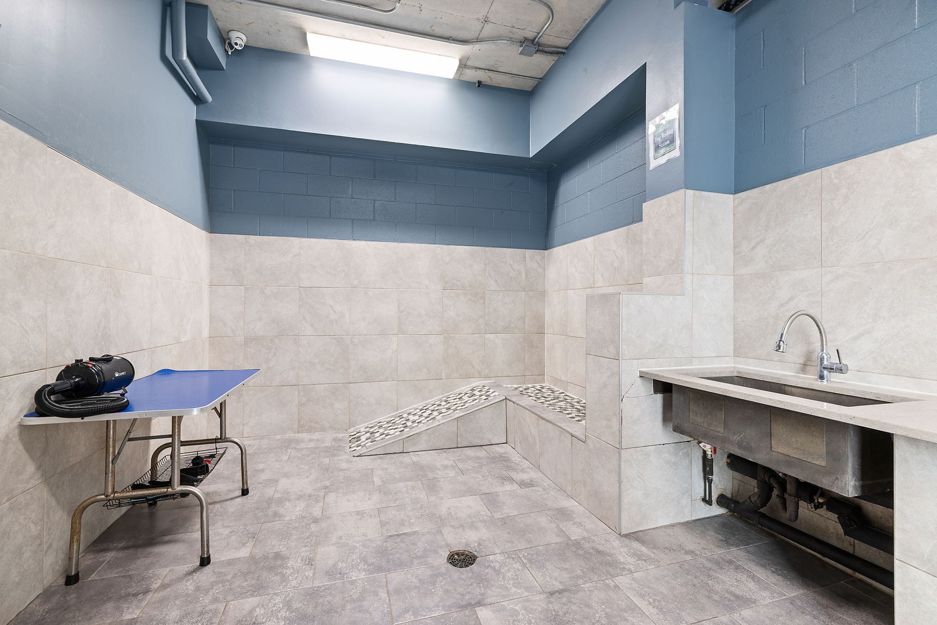 Small tiled washroom with sinks, a table, and blue-gray walls.