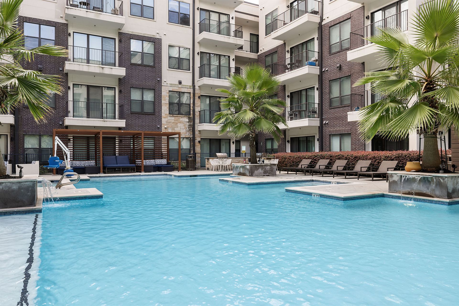 Apartment complex pool with lounge chairs, palm trees, and turquoise water