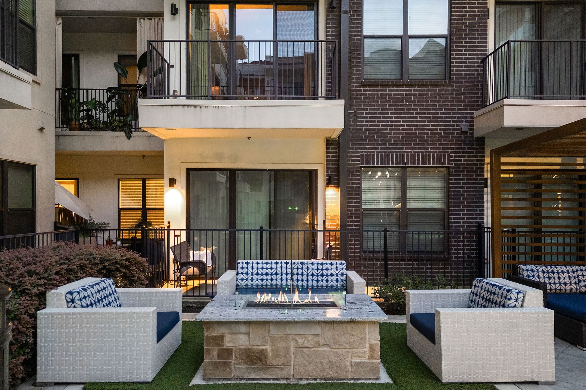 Modern apartment courtyard with white outdoor seating around a fire pit at dusk