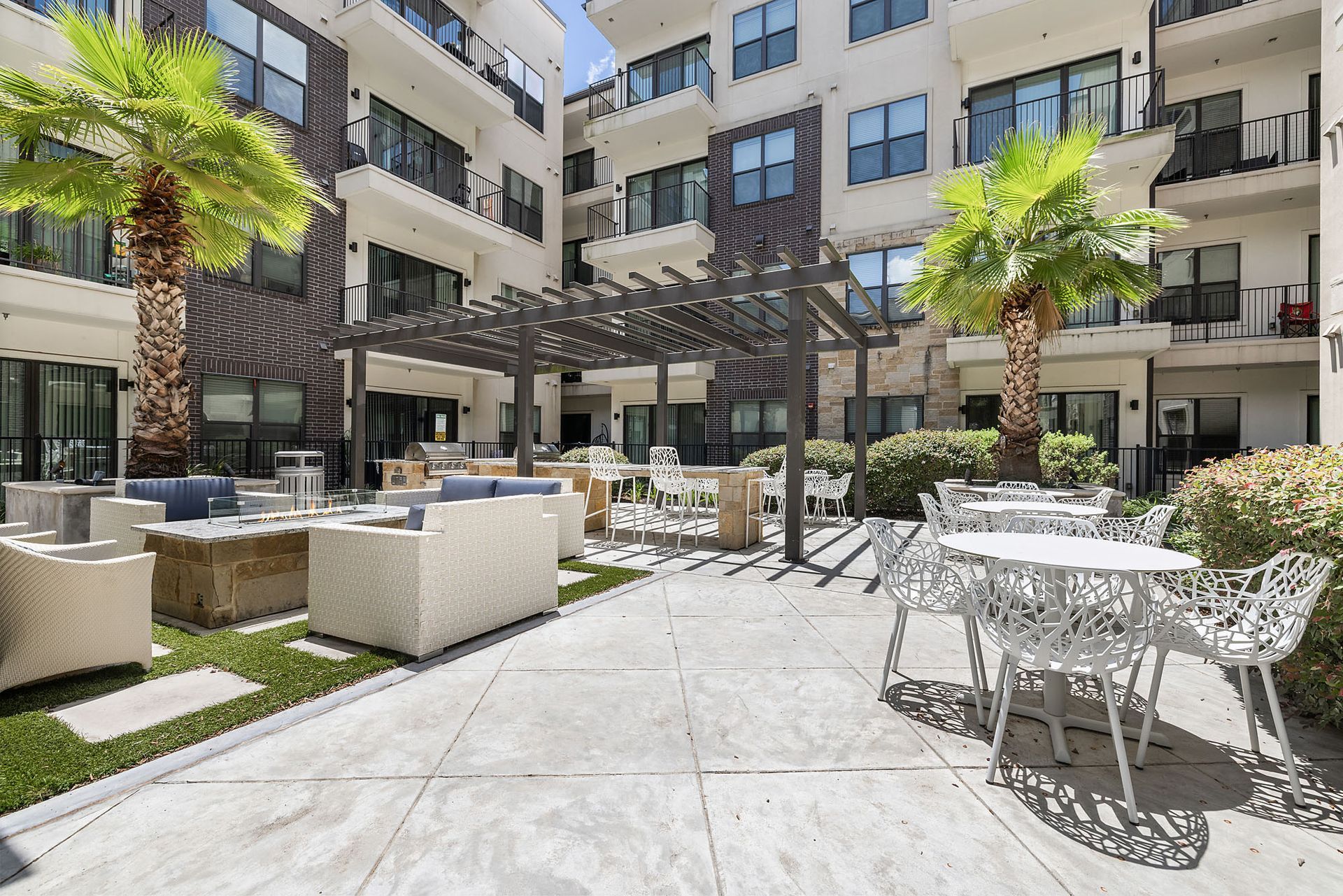 Sunlit apartment courtyard with patio seating, palm trees, and multi-story balconies