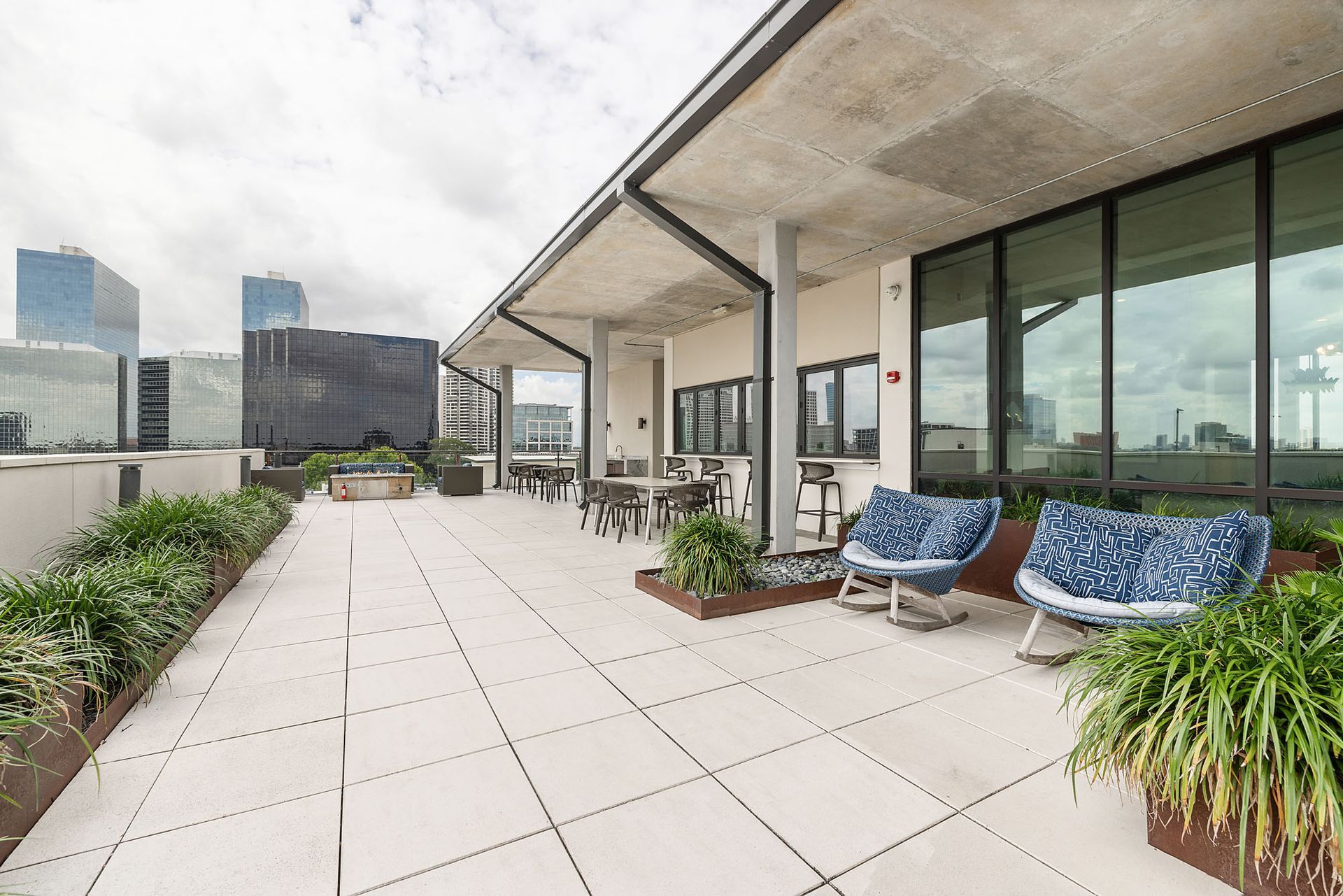 Rooftop terrace with blue lounge chairs, potted plants, and city skyline views