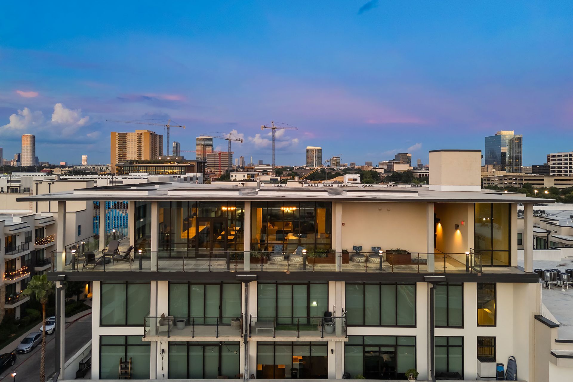 City rooftop terrace at dusk with city skyline and pink-blue sky.