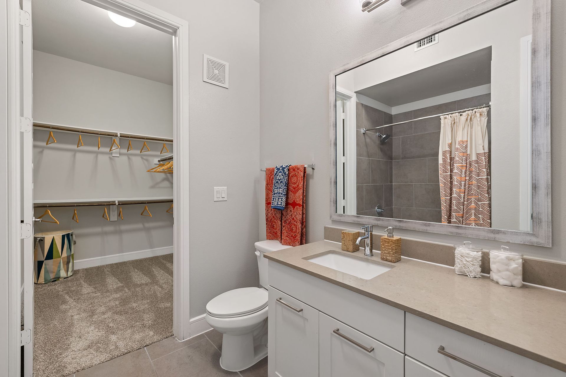 Modern bathroom with vanity, large mirror, and open walk-in closet beyond the doorway
