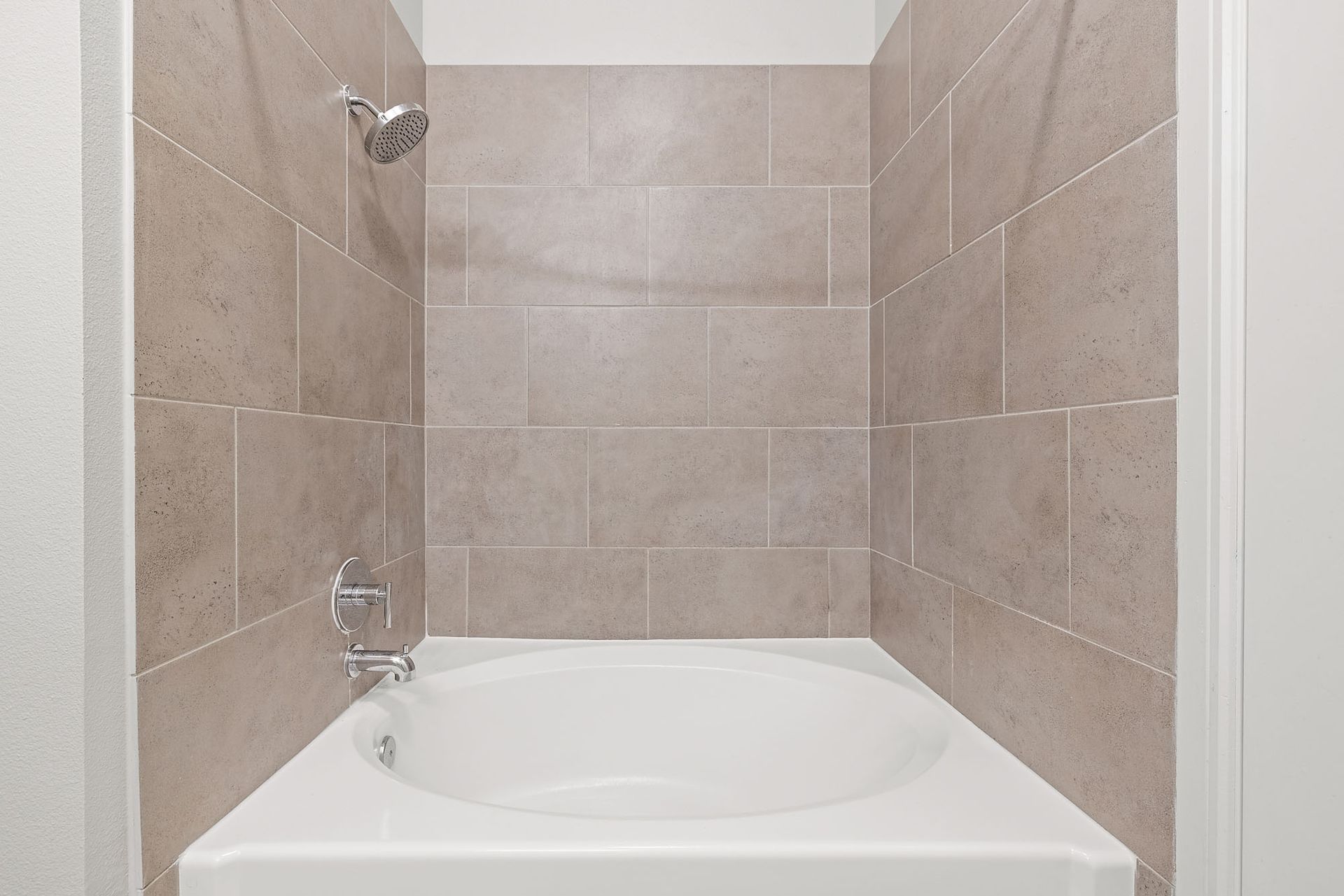 Small beige-tiled bathtub alcove with a white tub and chrome shower fixtures.