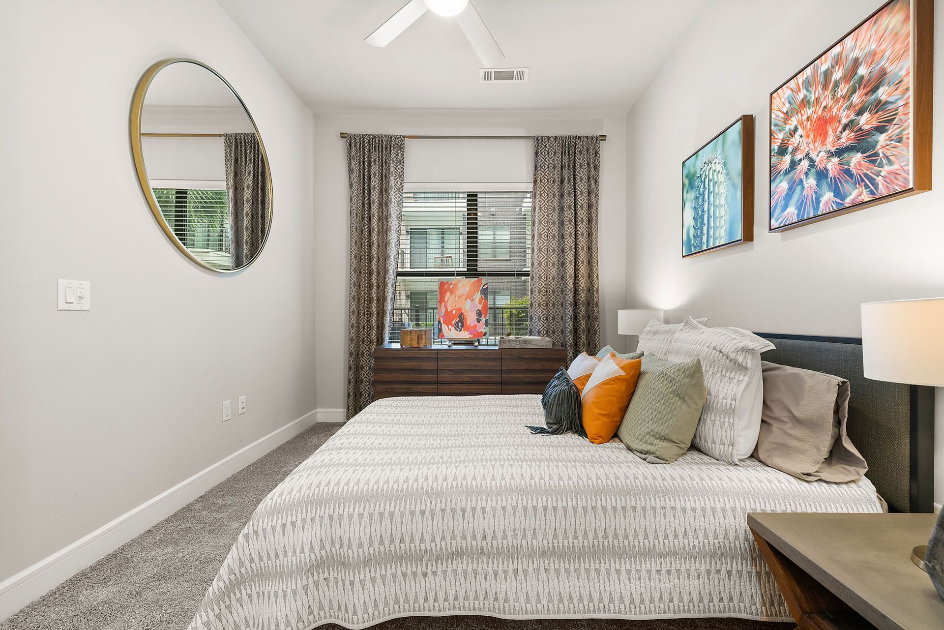 Neat bedroom with a bed, window seat, wall mirror, and colorful artwork.