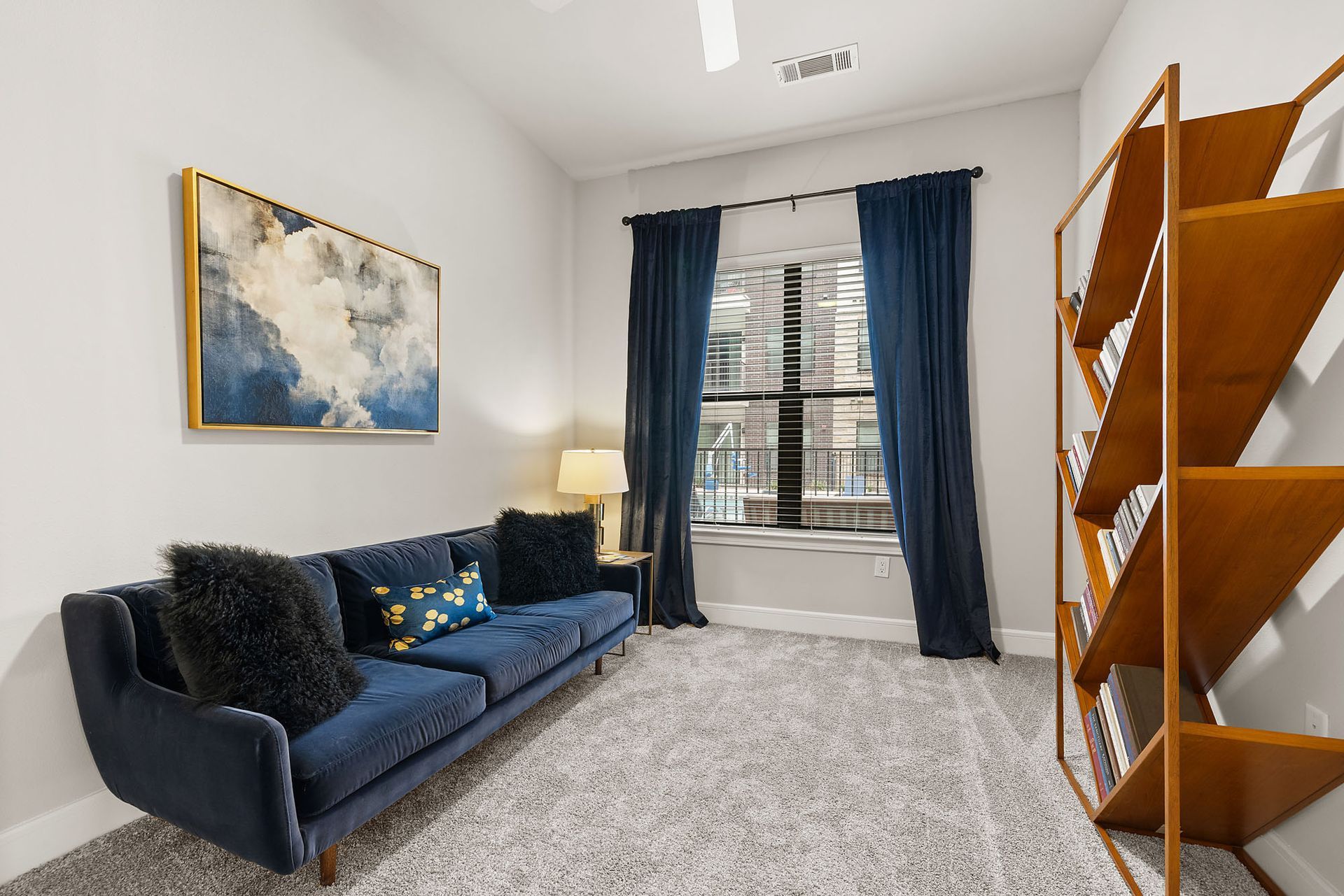 Bright living room with blue sofa, abstract wall art, navy curtains, and wooden shelving on the right