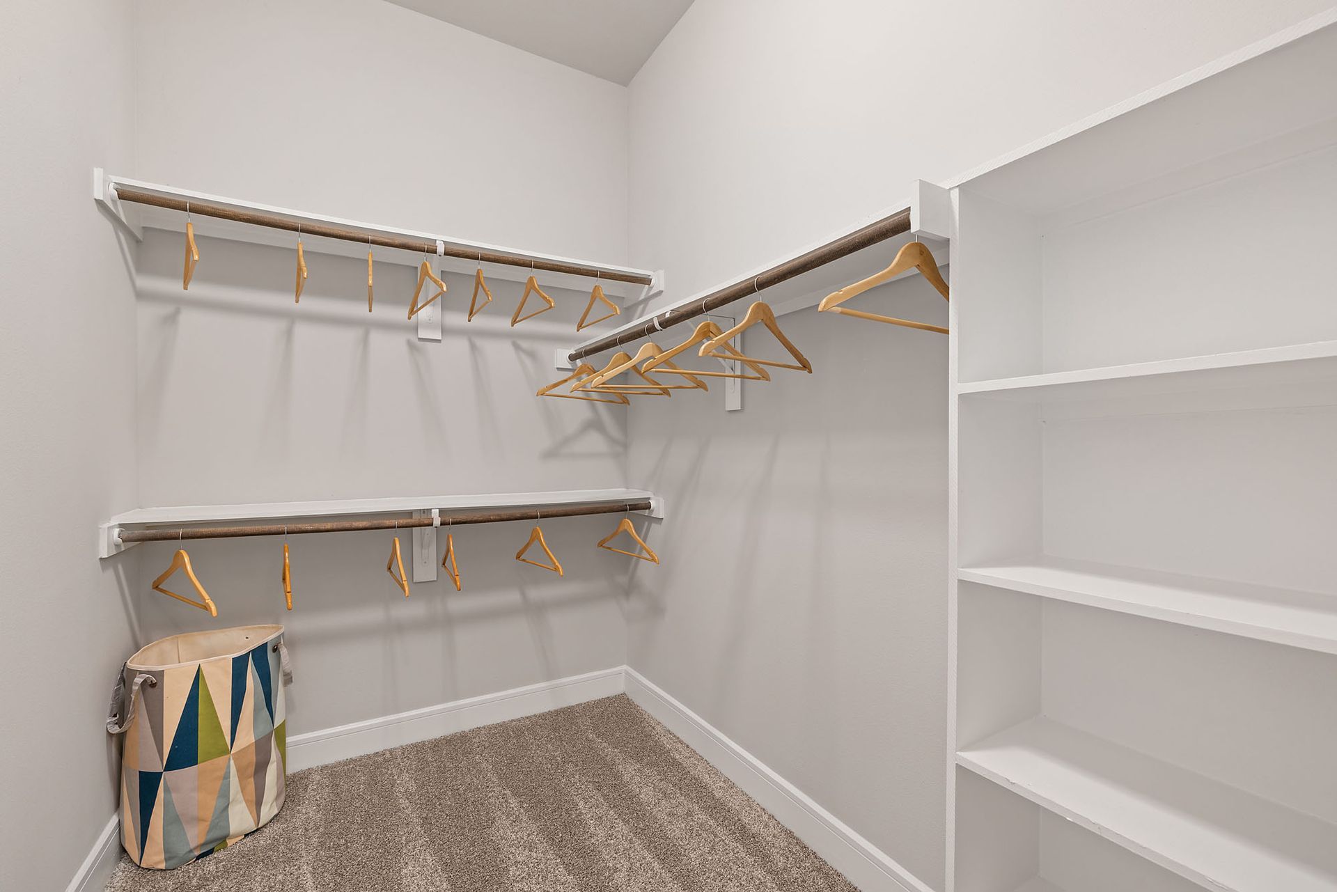 Empty walk-in closet with white shelves, hanging rods, and beige carpet.