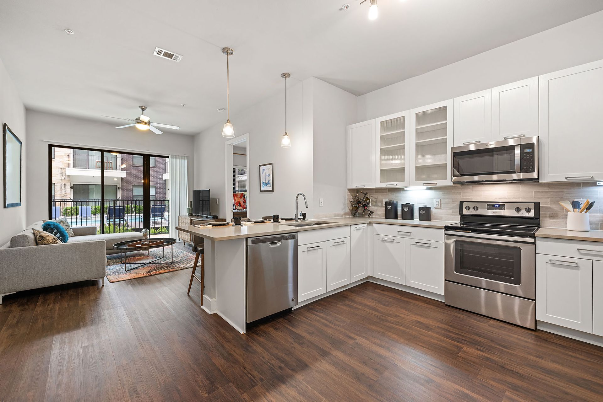 Open-plan modern kitchen and living room with white cabinets, stainless appliances, and hardwood floors.
