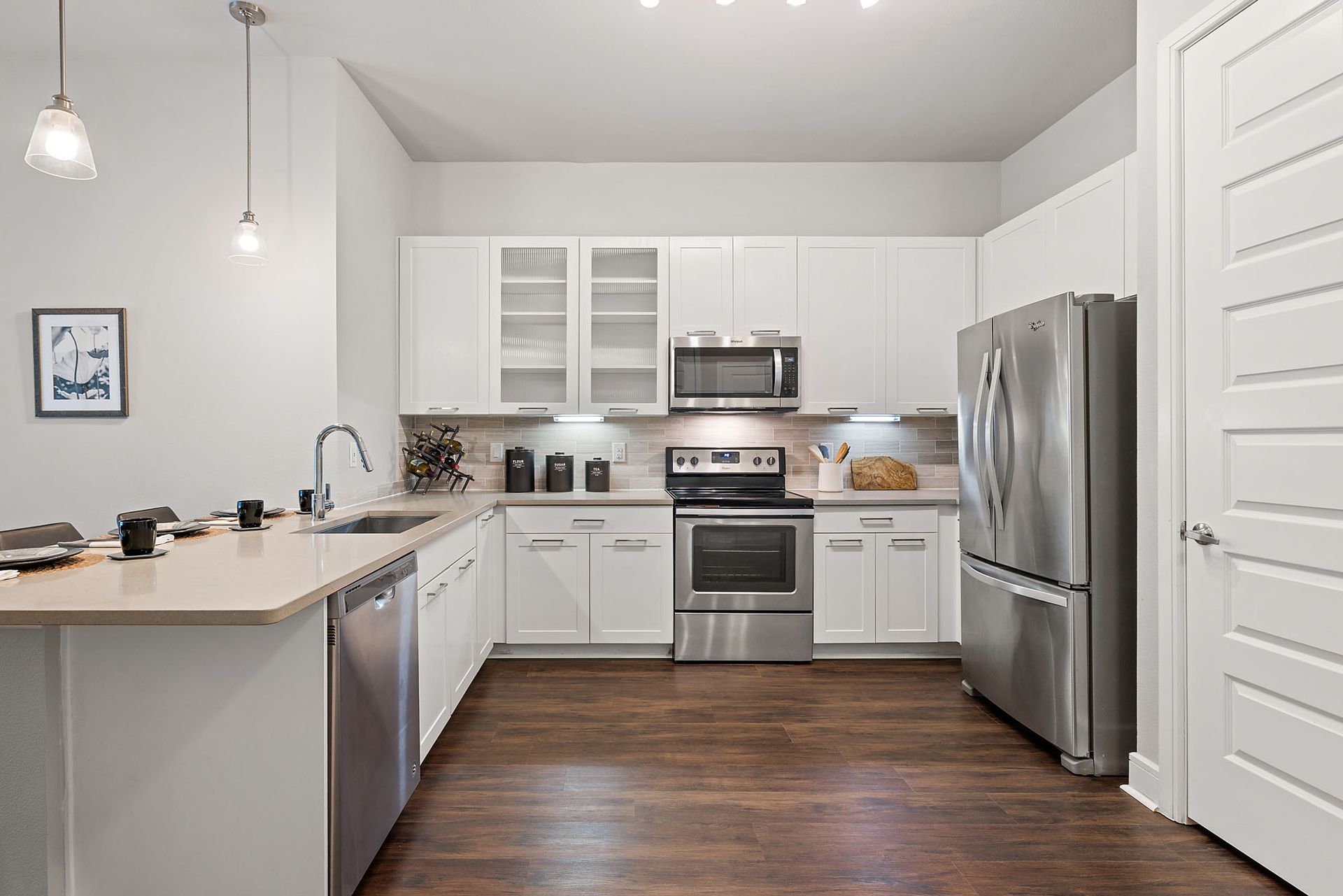 Modern white kitchen with stainless steel appliances, dark wood floors, and light countertops