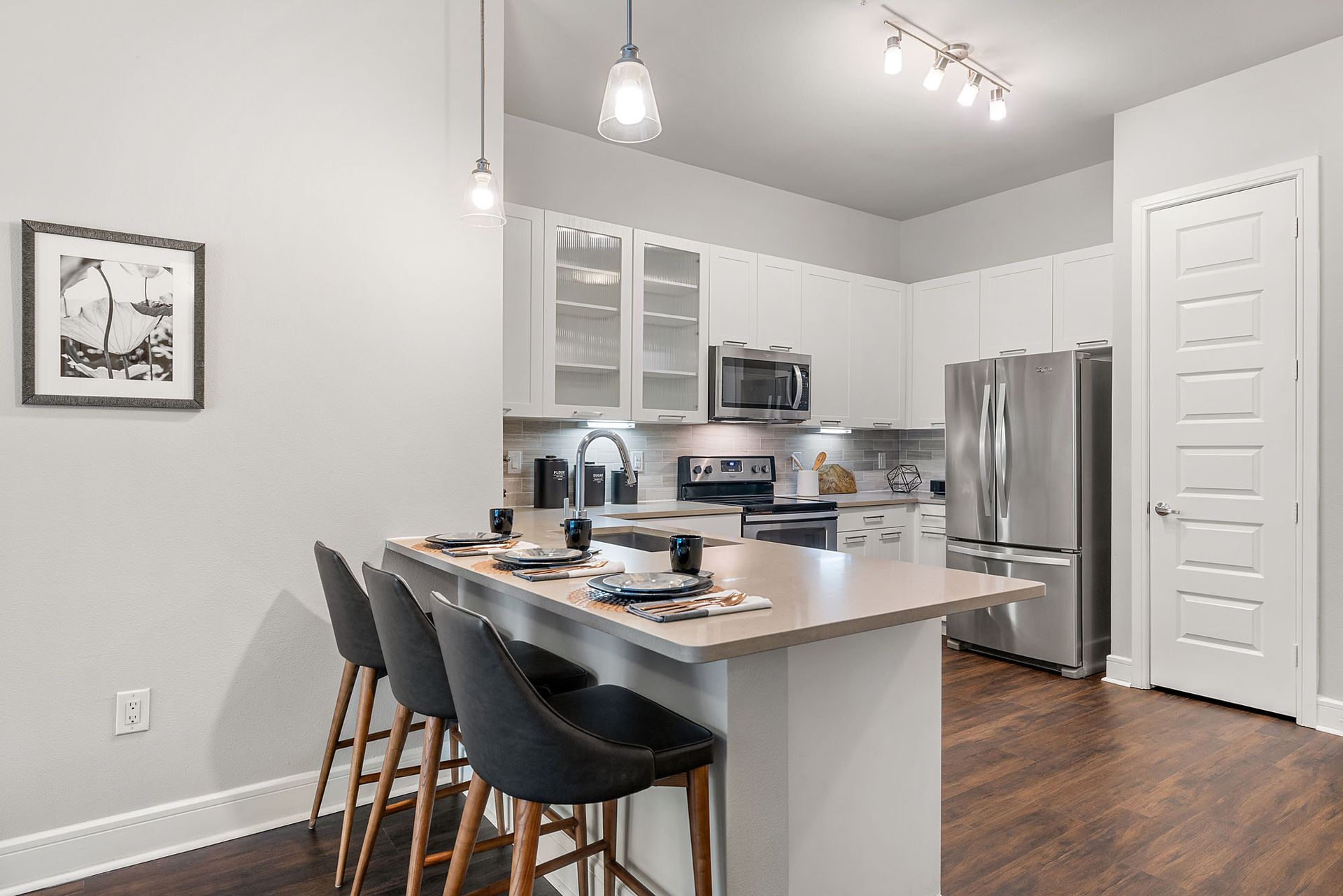 Modern kitchen with white cabinets, stainless appliances, island seating, and hardwood floors
