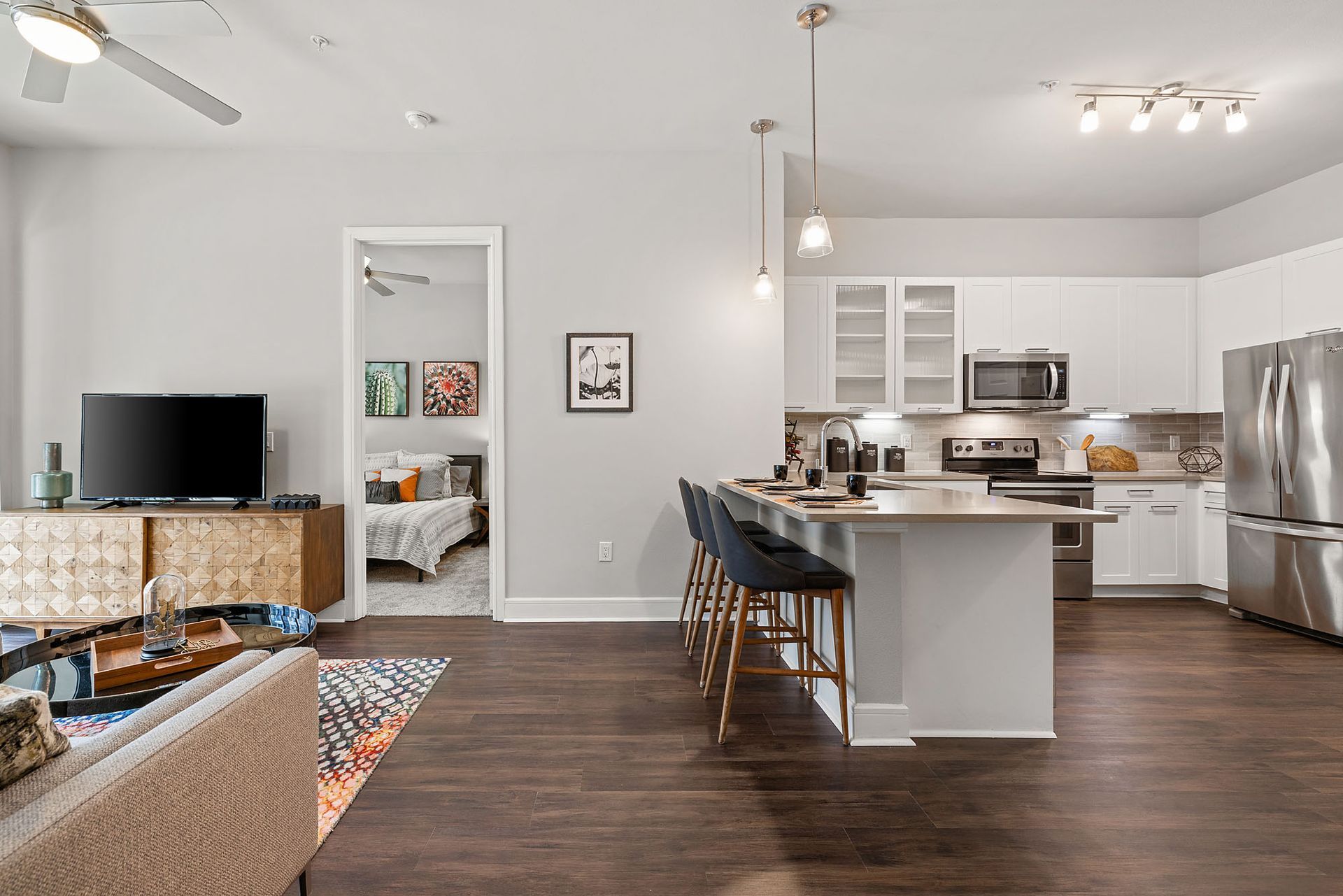 Open-concept living room and kitchen with gray walls, dark wood floors, and stainless steel appliances.