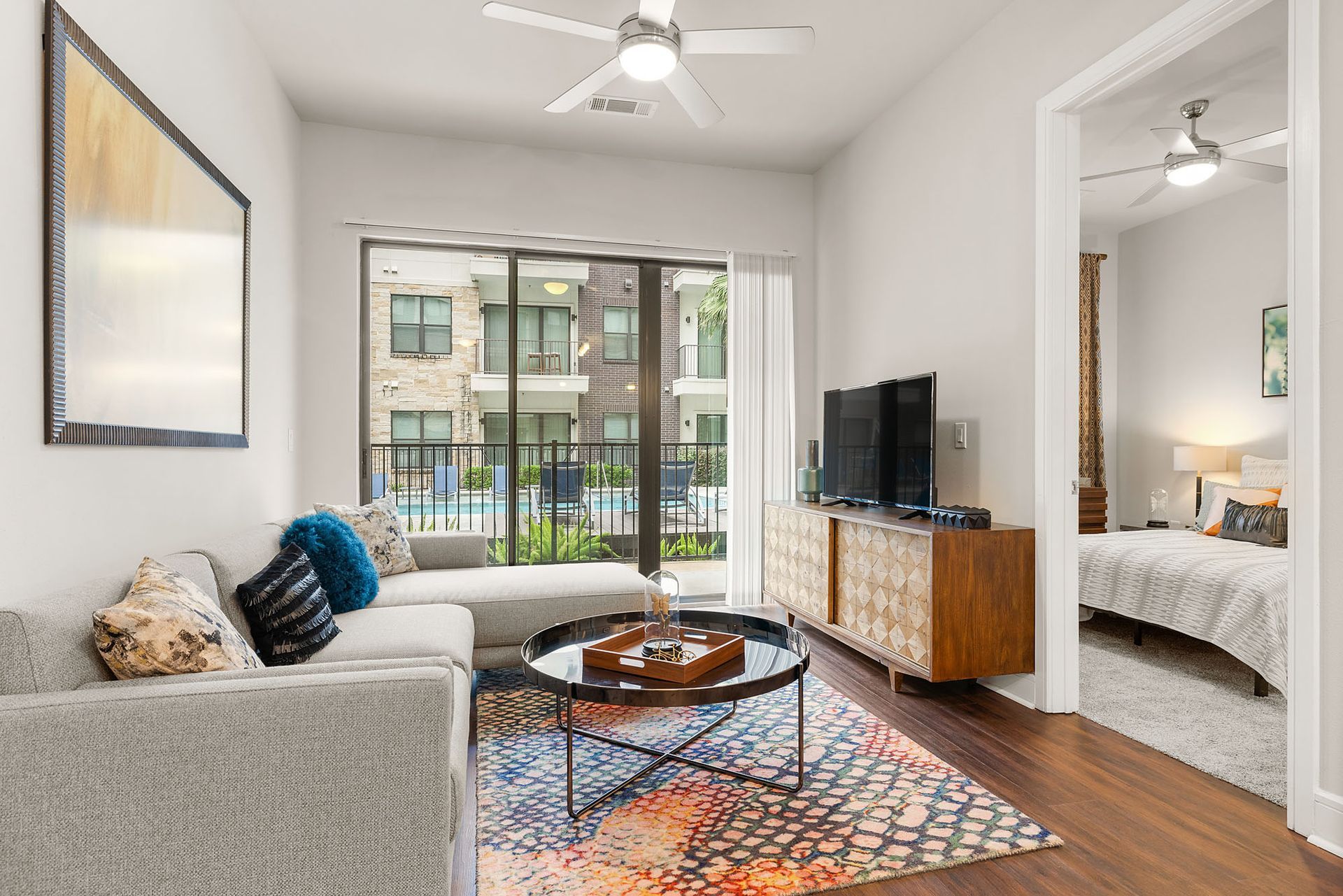 Bright modern living room with gray sofa, TV, patterned rug, and balcony view through large windows