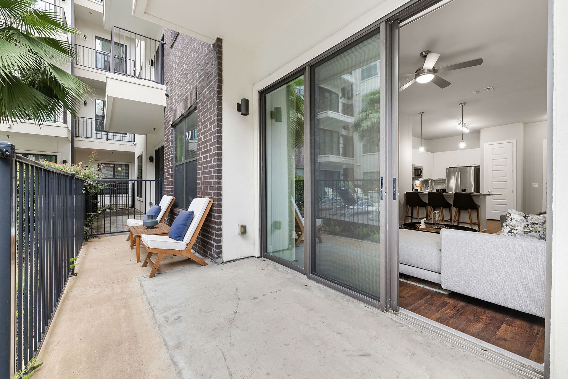 Apartment patio with two chairs, sliding glass door, and view into a bright living room
