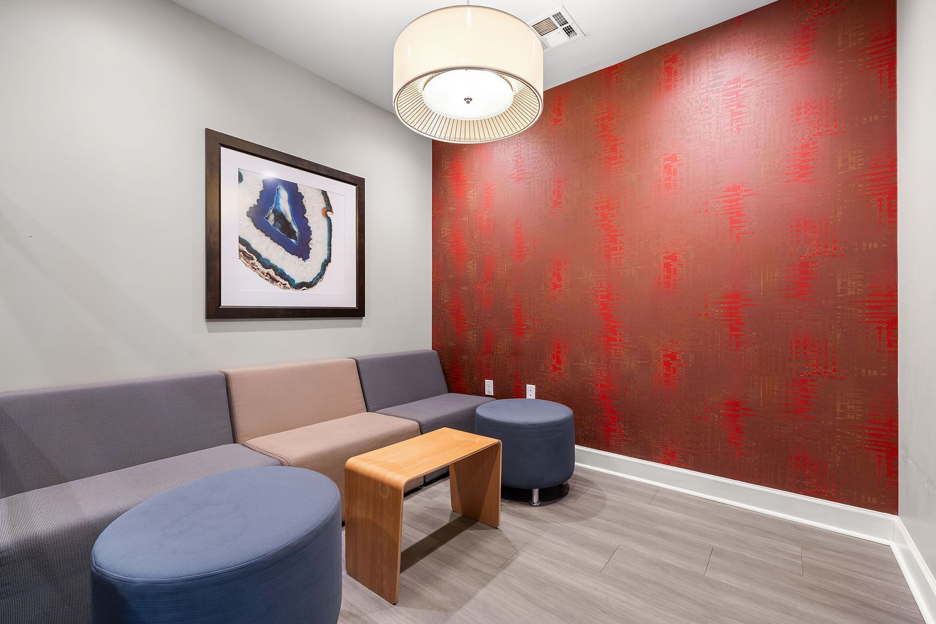 Modern lounge with gray and red accent walls, blue ottomans, beige sofa, and a round pendant light.
