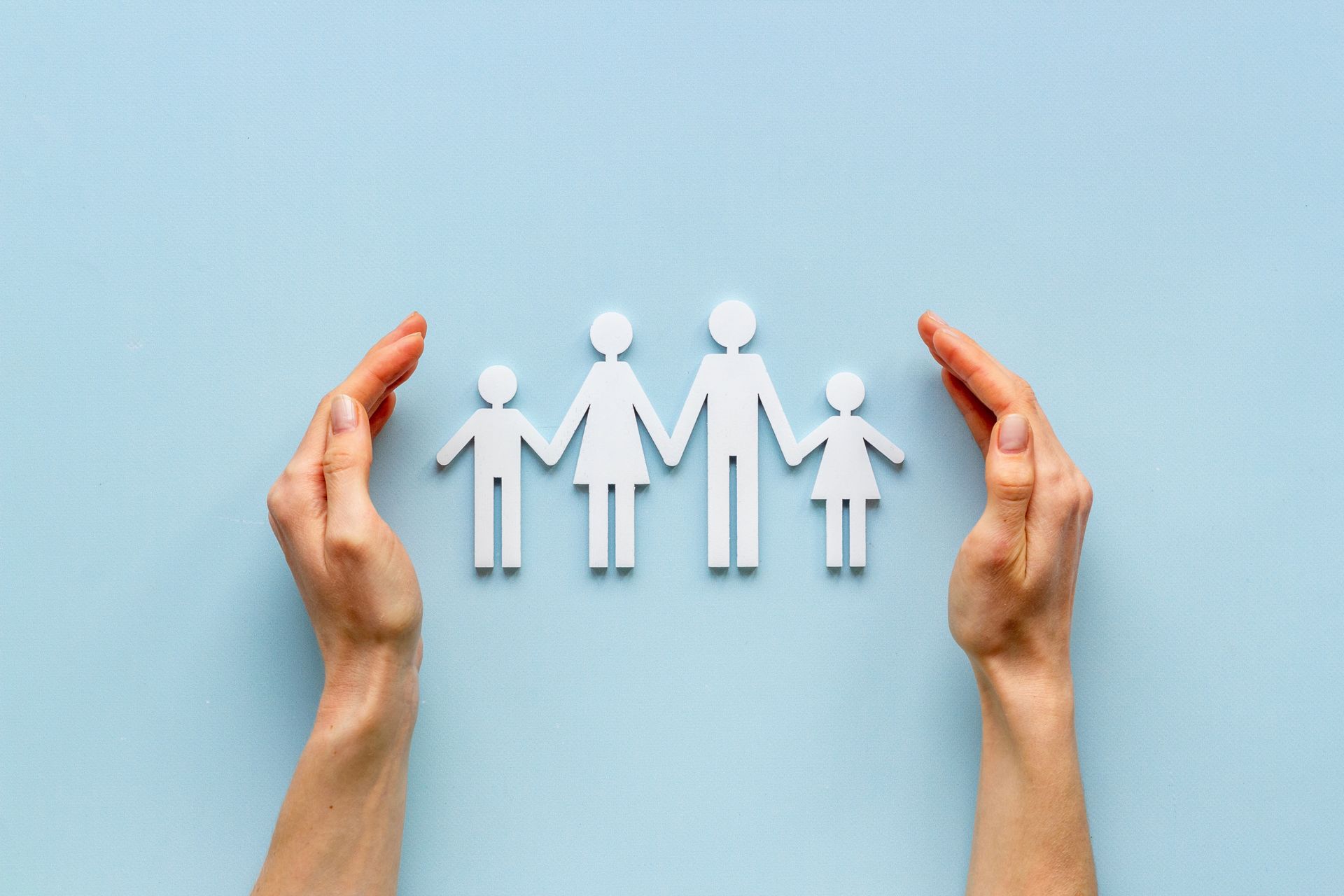 Hands cupping a paper cutout of a family on a light blue background.
