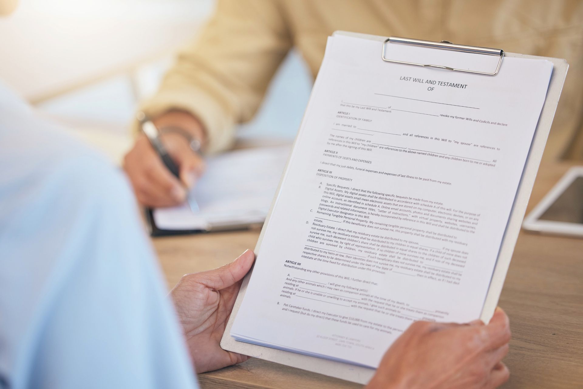 Person holding a clipboard with document; another person in background writes on paper.
