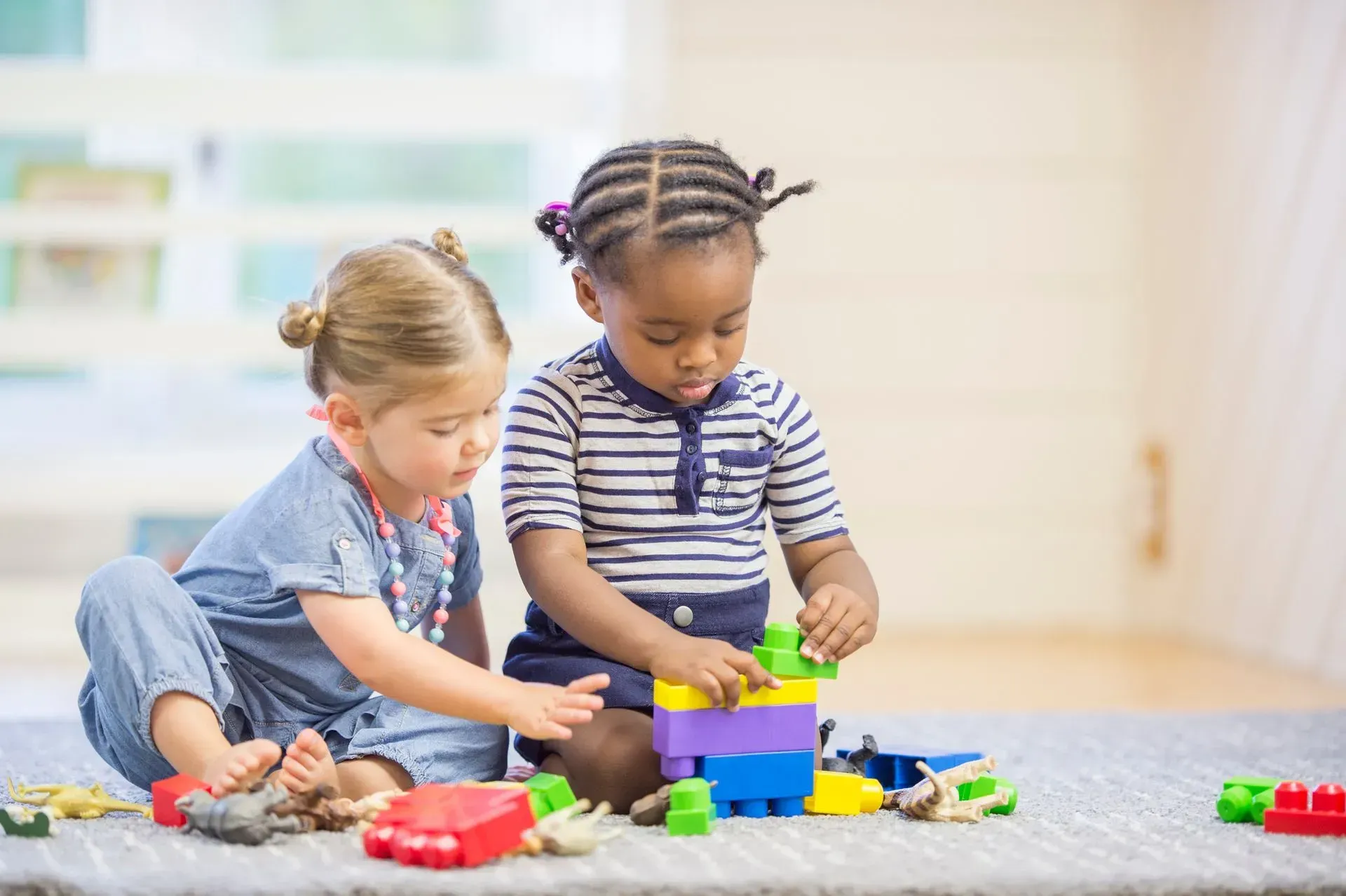 Two little girls are playing with blocks on the floor.