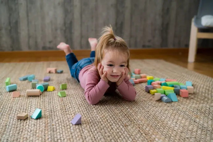 A little girl is laying on the floor playing with wooden blocks.