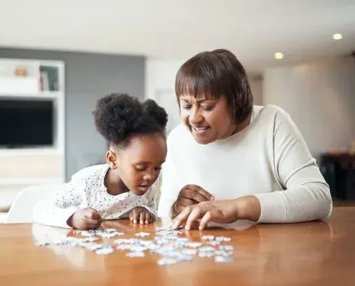 A woman and a little girl are sitting at a table playing with puzzles.