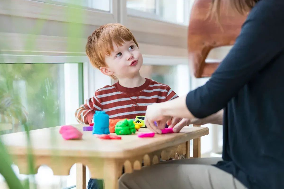 A woman is sitting at a table with a child playing with play dough.