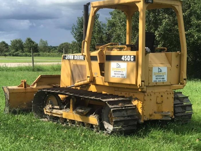 Yellow Caterpillar 450G bulldozer parked in a grassy field under cloudy skies