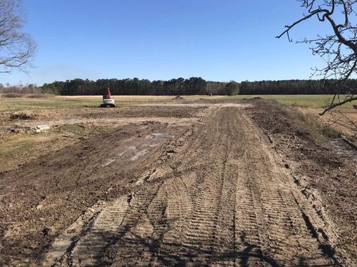 Dirt road through an open field under a clear blue sky, with a small tractor in the distance.