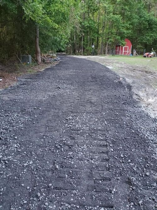 Gravel road through a wooded area with a red structure in the distance