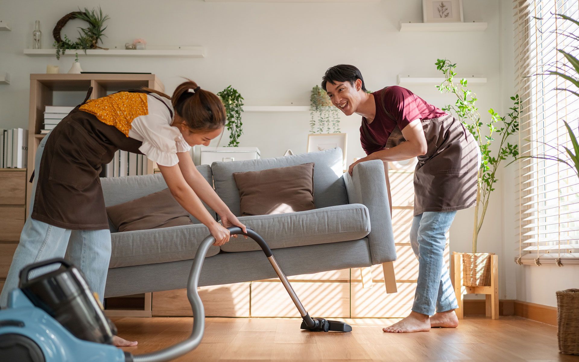A man and a woman are cleaning a living room with a vacuum cleaner.