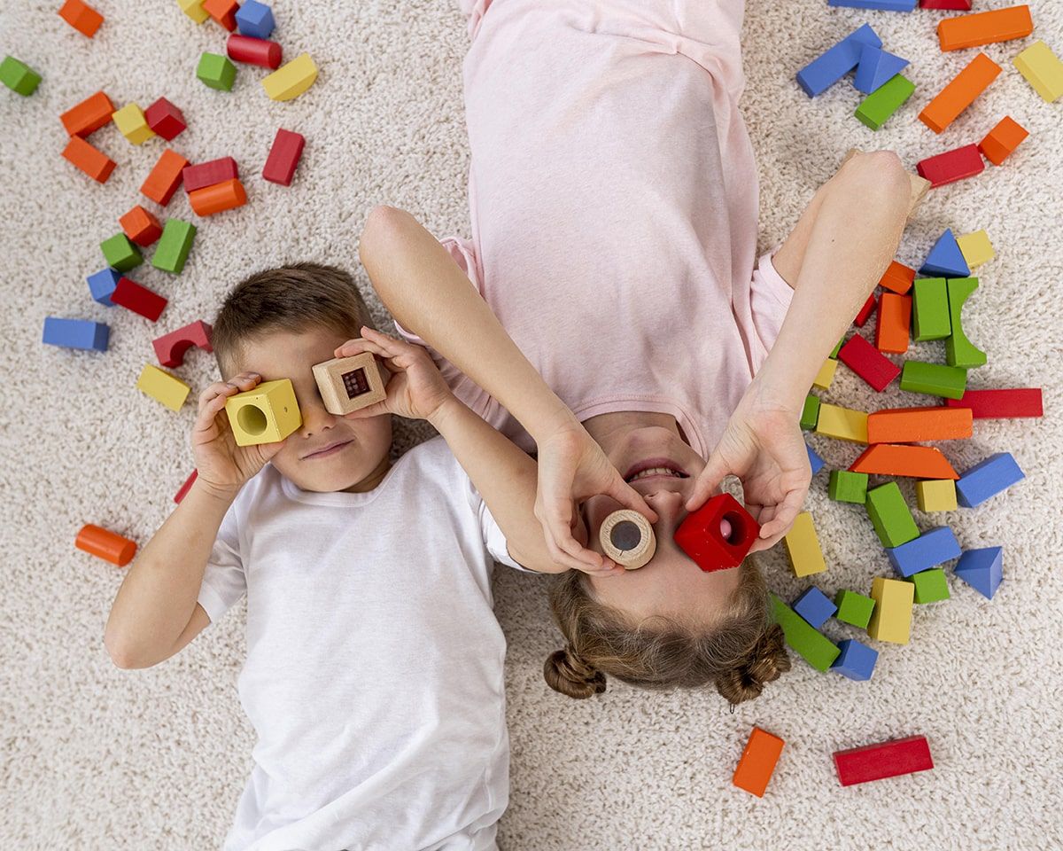 Um menino e uma menina estão deitados no chão brincando com blocos.