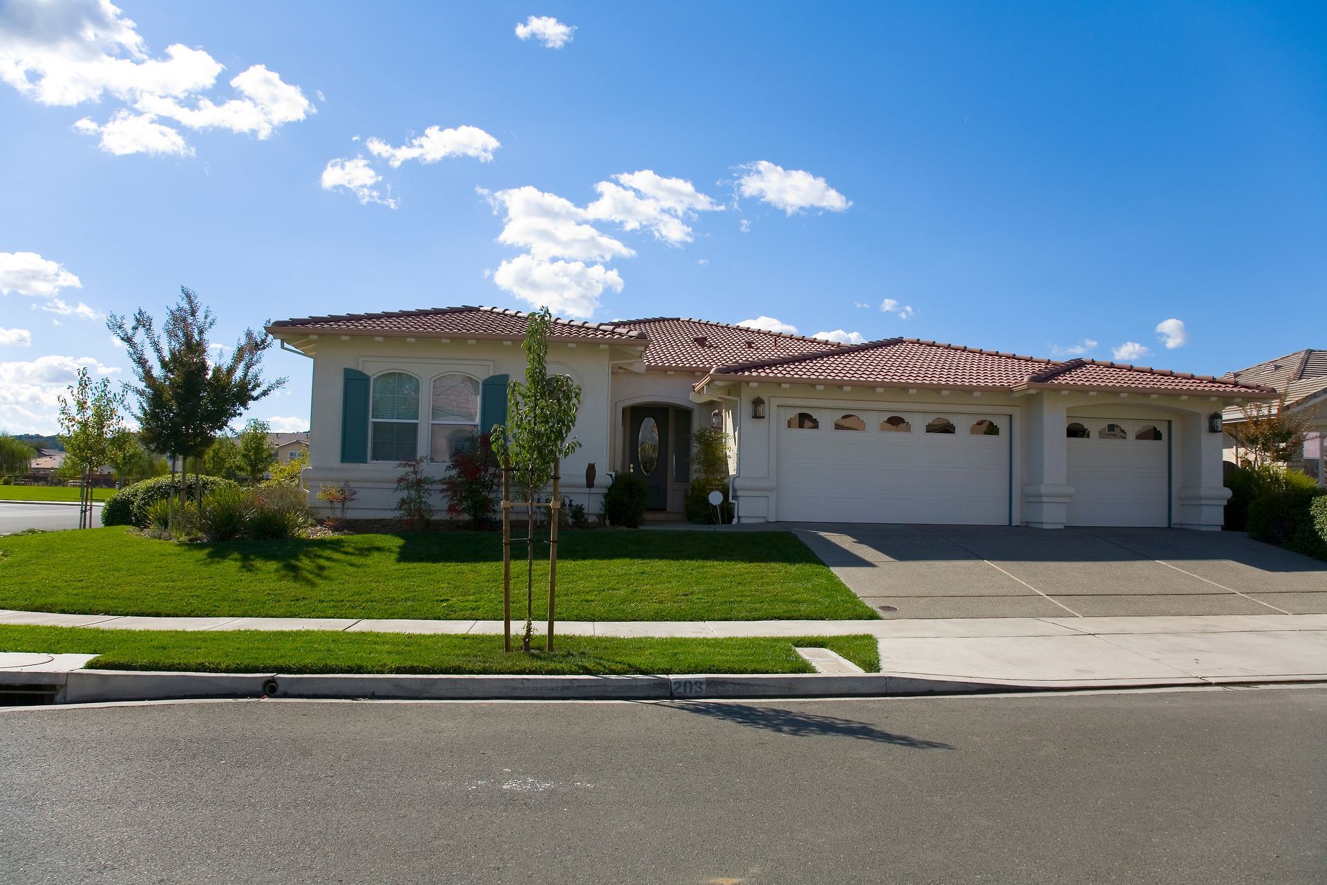 Single-story suburban house with a red tile roof, white garage, and a green lawn under a blue sky.