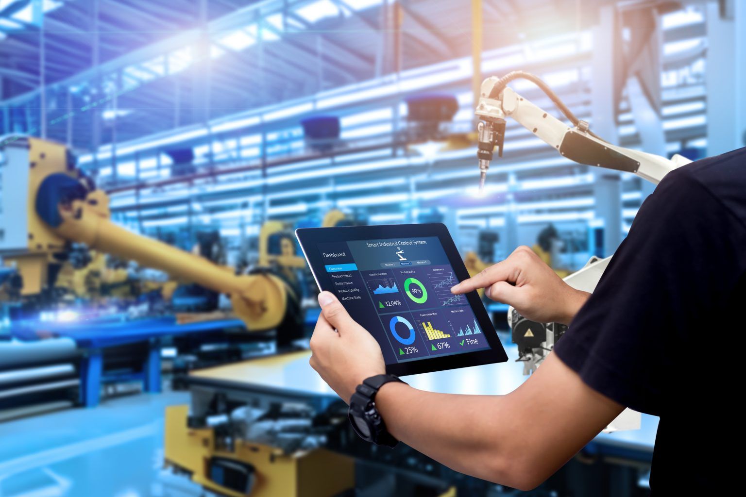 Person using a tablet in a factory setting, with robotic arms visible.