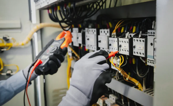 Hands wearing gloves using multimeter on electrical panel.